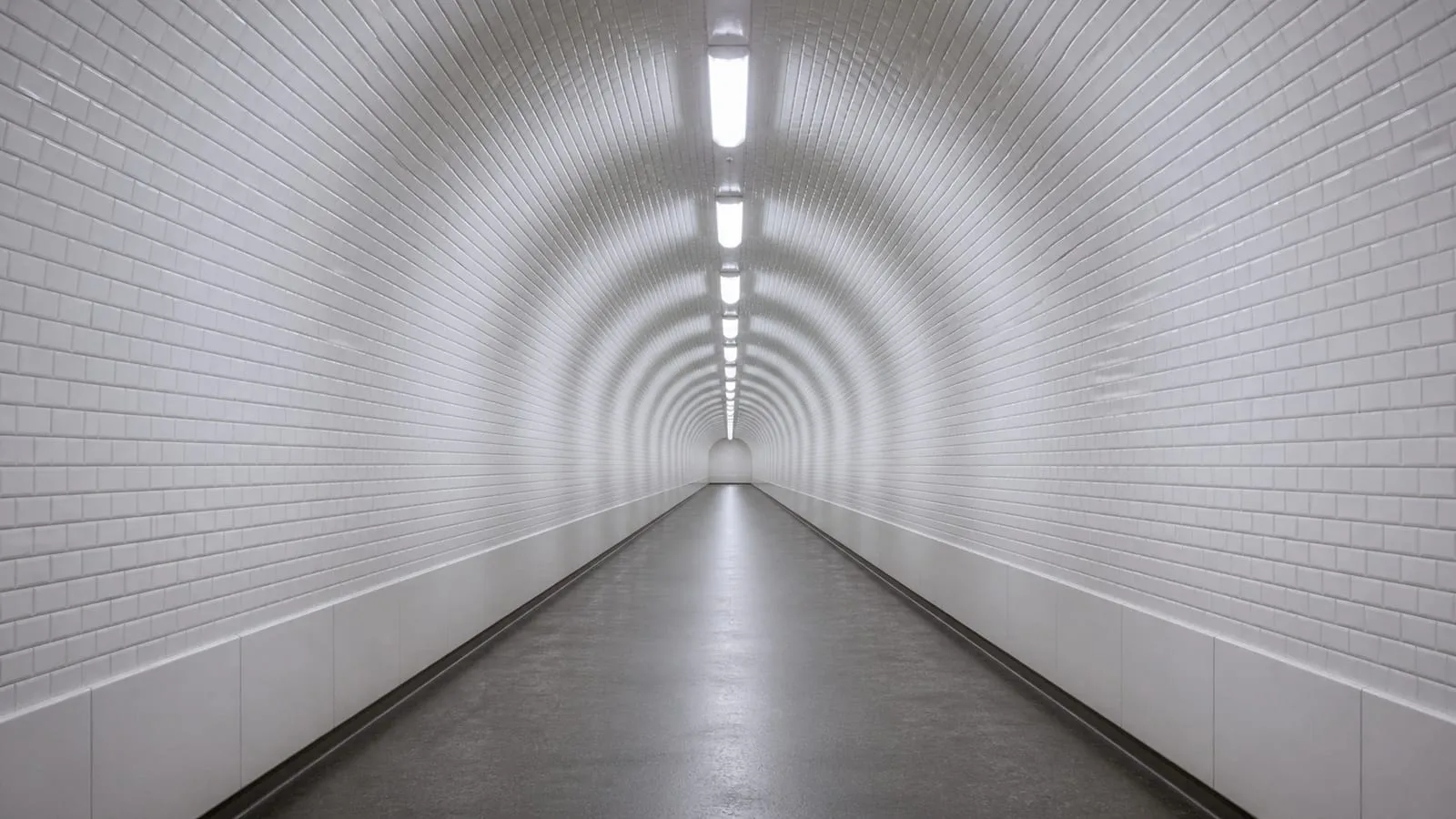 Un long couloir de métro carrelé de blanc, entièrement vide, en perspective.
