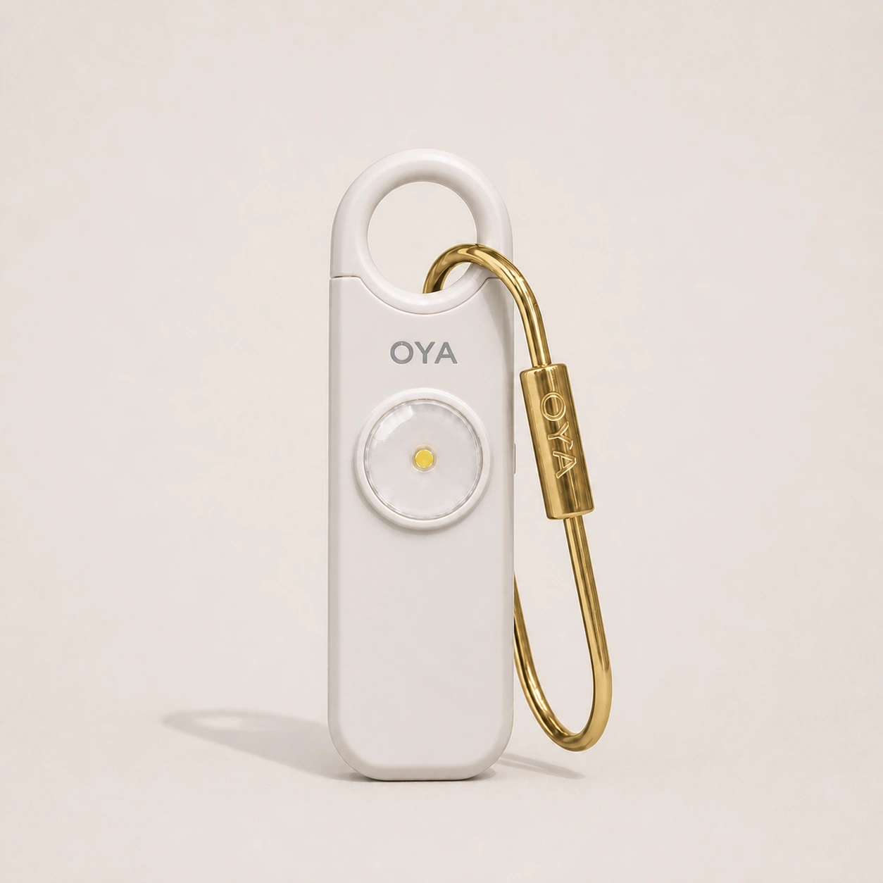 L’alarme personnelle OYA en Pearl Sand avec son clip doré, sur un fond assorti à la teinte